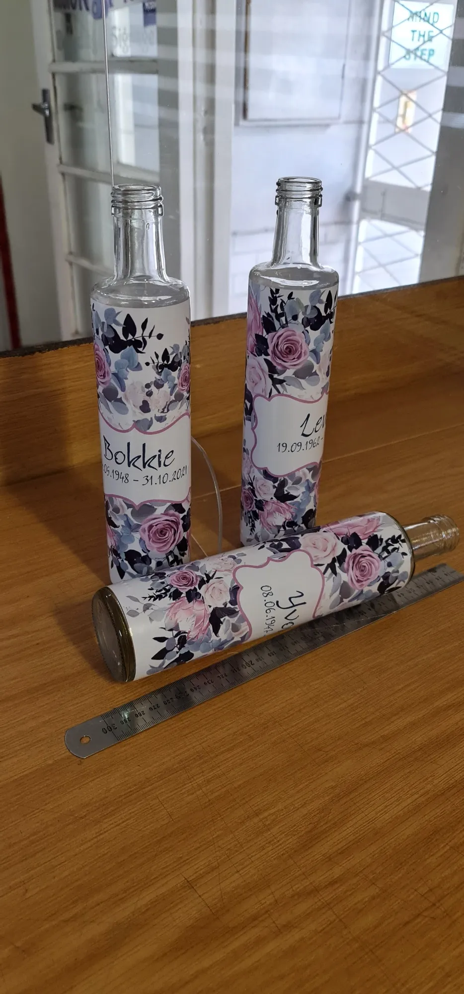 Three glass bottles wrapped in custom-printed floral labels with personalised lettering.